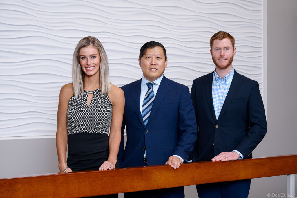 Three professionals at a Houston oral surgery practice pose for a corporate group photo in a modern office interior.
