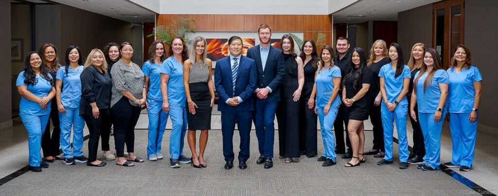 Large corporate group of medical staff in blue scrubs and business attire pose together for a professional team photo in Houston.