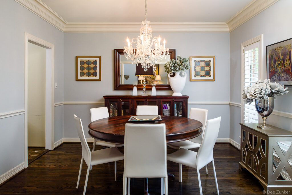 Elegant Houston dining room with crystal chandelier, round walnut table, white modern chairs, and classic crown molding interior design.