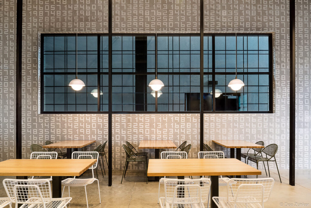 Modern restaurant dining room with wood tables, wire chairs, pendant lights, and a grid window wall with number-patterned tile backdrop