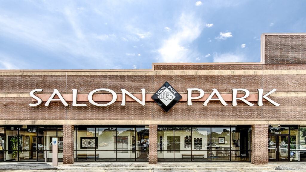 Brick exterior facade of a Houston hair salon retail strip center featuring large dimensional signage under a partly cloudy sky