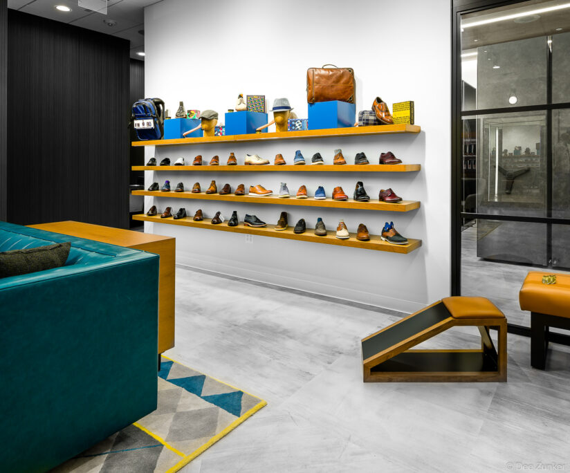 Wide-angle interior of a Houston shoe store showing wall-mounted shelves with men's dress shoes, accessories, and a teal sofa seating area.