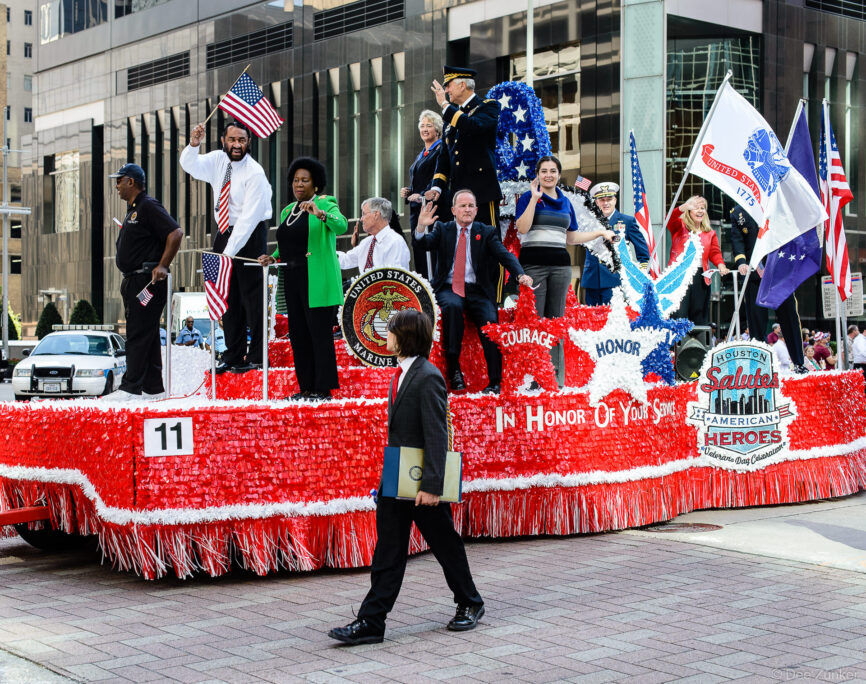 Decorated patriotic parade float honoring US military veterans rolls through downtown Houston during Veterans Day celebration event.