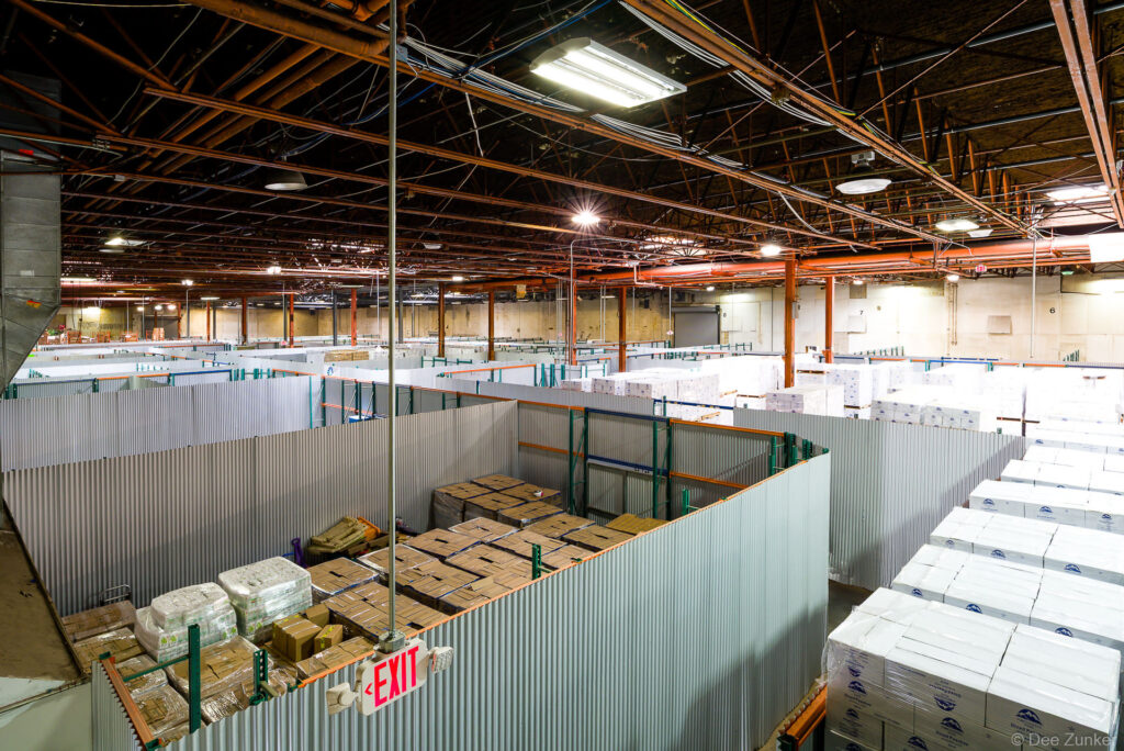 Aerial view of large Houston warehouse interior with corrugated metal storage bays stacked with palletized boxes and industrial ceiling lighting.