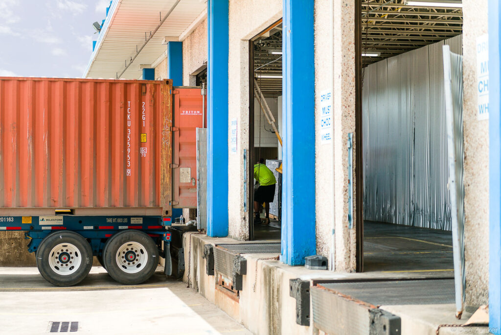 Workers unload a red shipping container at an industrial warehouse loading dock in Houston, TX, photographed for commercial portfolio.