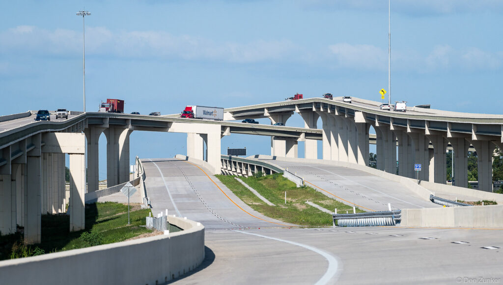 Pre-opening aerial view of Hwy 59 and Hwy 99 interchange showing multilevel concrete flyover ramps and light traffic, Houston Texas