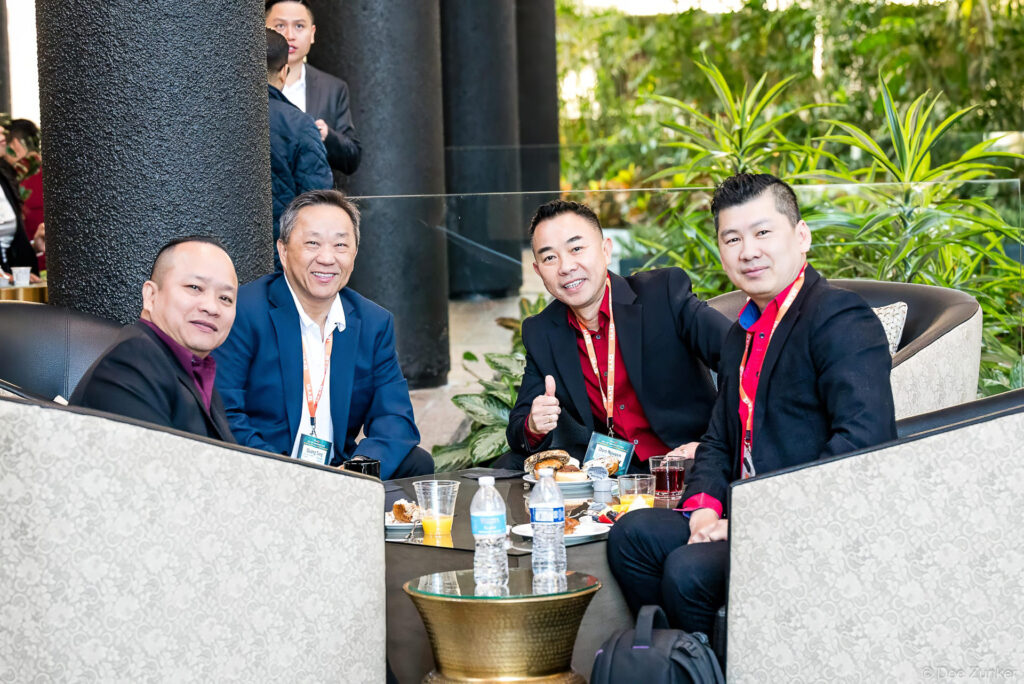 Four male conference attendees smile and give thumbs up at a lounge table during an IAA kick-off meeting networking breakfast.