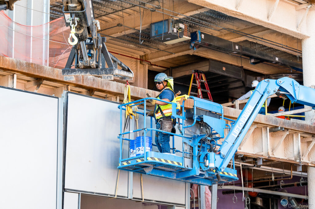 Construction worker in boom lift installs exterior facade panels at IAH Terminal B during active commercial construction progress documentation.