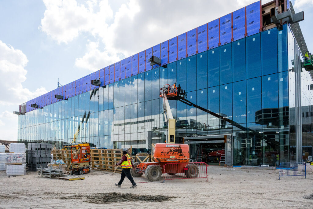 Construction crew and boom lift working on glass curtain wall facade installation at IAH Terminal B, Houston airport expansion project.