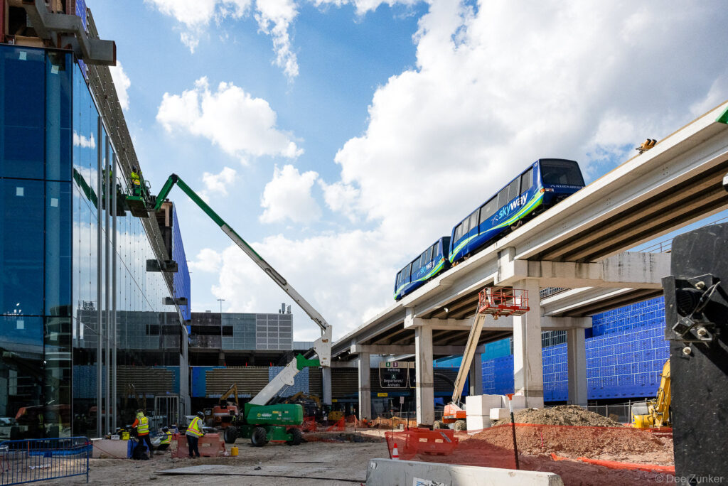 Skyway automated people mover on elevated guideway at IAH Terminal B construction site, with boom lifts and workers on active jobsite.