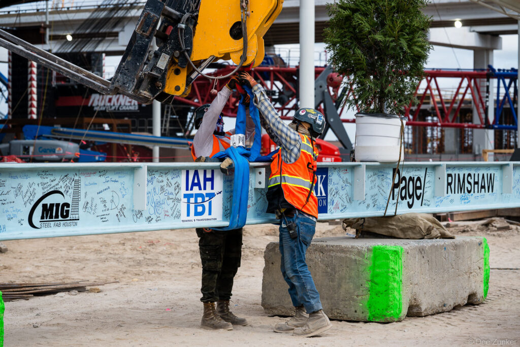 Two construction workers guide a signed steel beam during the IAH Terminal B Transformation topping out ceremony at Houston Intercontinental Airport.