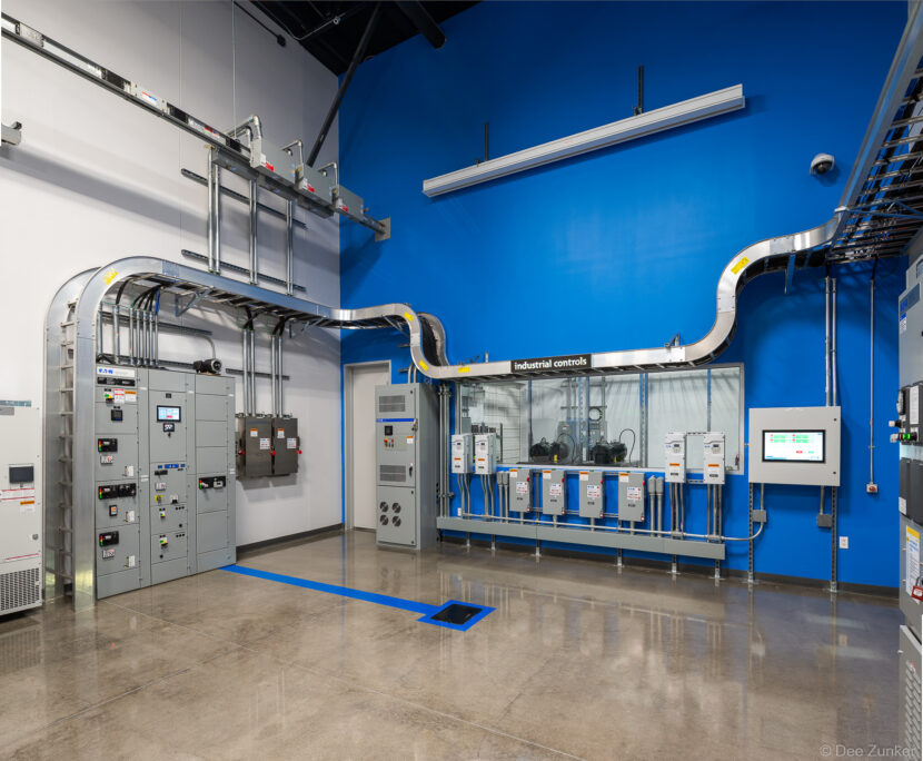 Industrial electrical control panels and conduit systems displayed in a modern showroom with blue accent walls, Houston commercial interior.