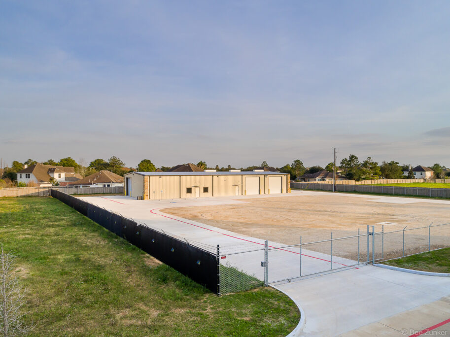 Aerial view of a metal warehouse facility with large garage doors, concrete apron, and gravel yard in northwest Houston, TX.