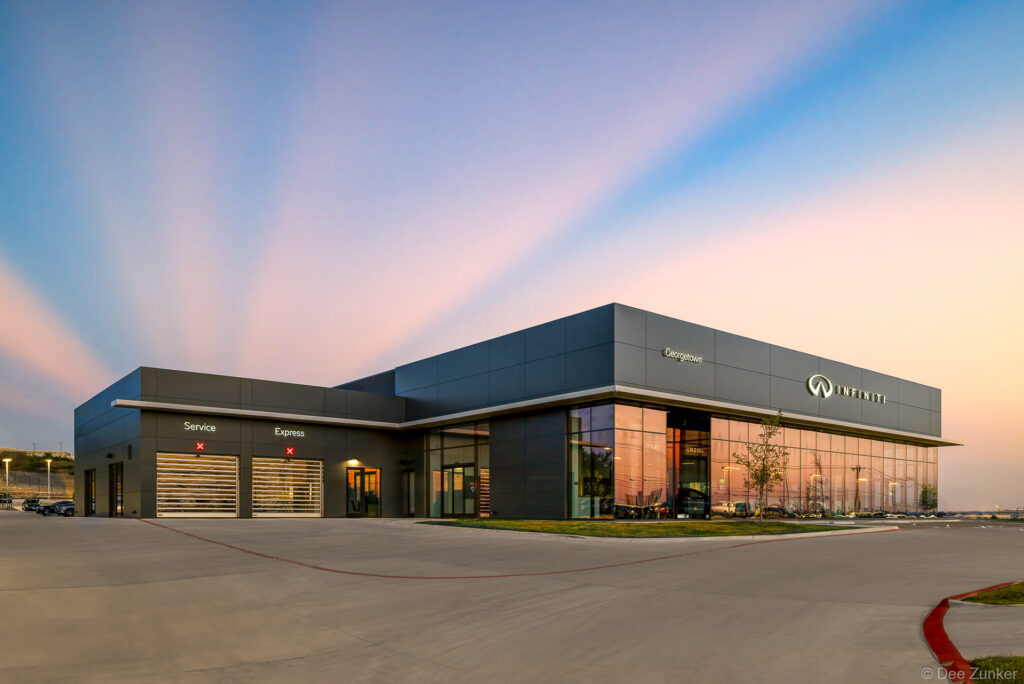 Luxury automotive dealership exterior at twilight in Georgetown Texas featuring floor-to-ceiling glass showroom and modern facade architecture
