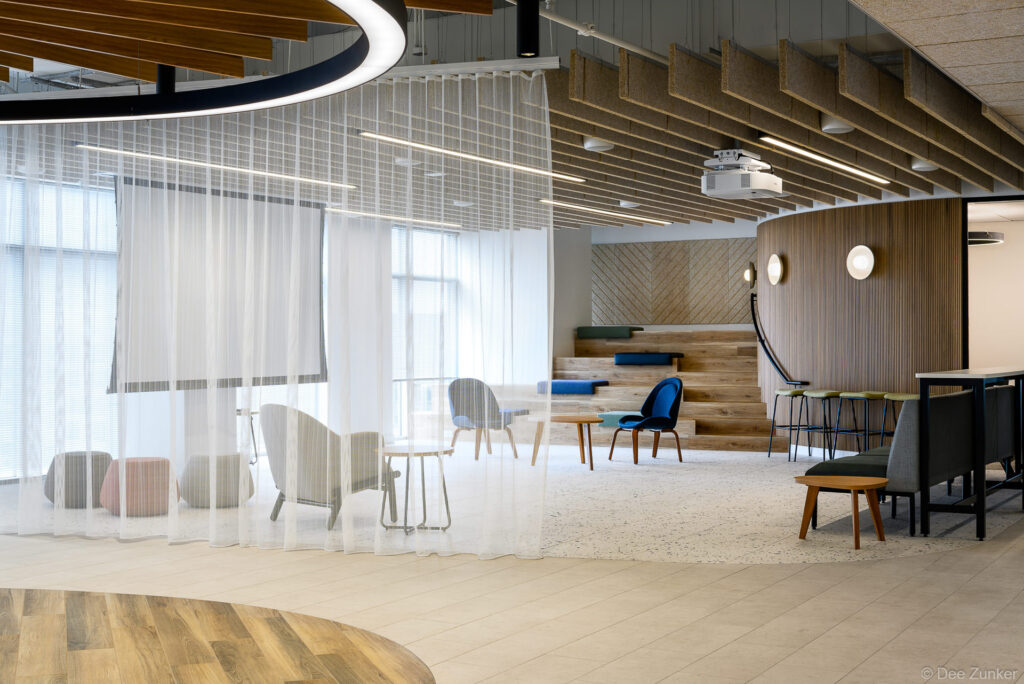 Modern corporate office interior with sheer curtain dividers, wood accent ceiling, terrazzo flooring, and flexible collaborative seating areas