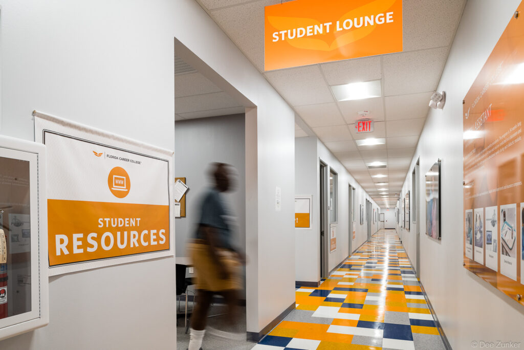 Bright college hallway with orange and blue checkered floor, student lounge sign, and student resources room in Southwest Houston
