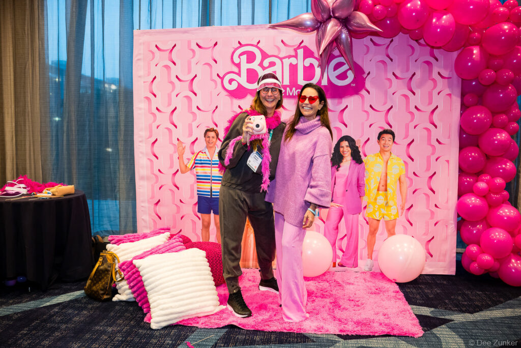 Two conference attendees pose at a pink Barbie-themed fundraiser photo booth at the INTA Leadership Meeting corporate event.