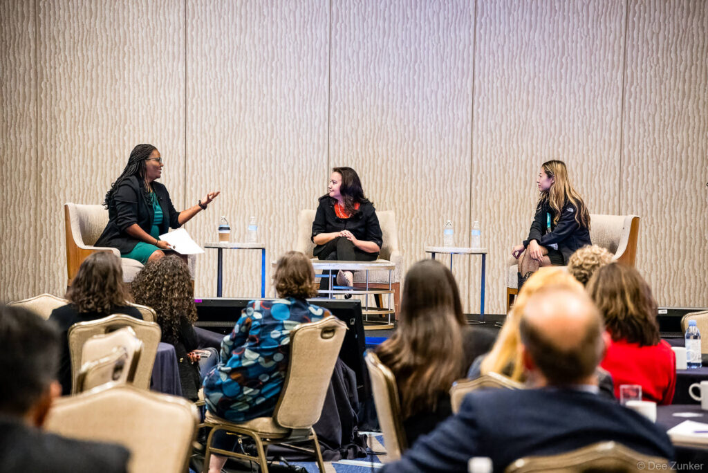 Three women seated on stage during a corporate conference panel discussion on future-proofing teams, with an engaged audience in the foreground.