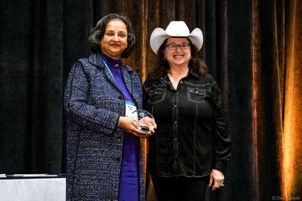 Two professional women pose together at an INTA Leadership Meeting opening awards ceremony, one holding a crystal trophy award.
