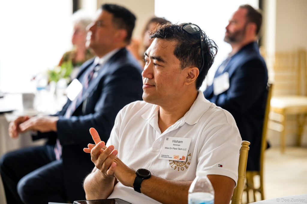 Male conference attendee applauds during Iron Mountain Houston corporate event, wearing name badge, sunglasses on head, white polo shirt.