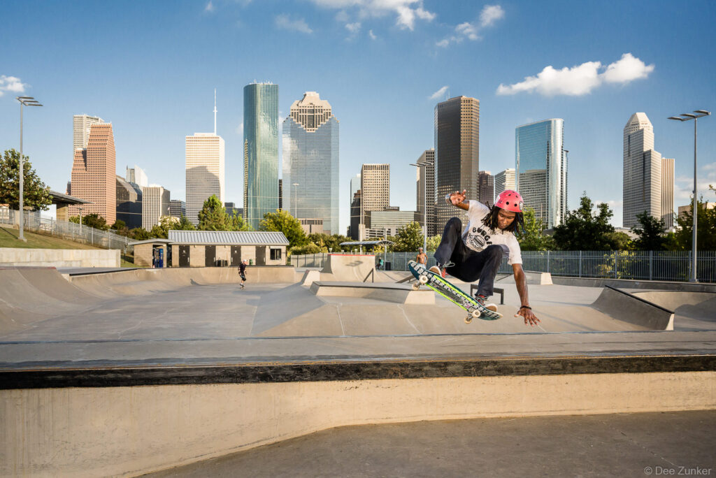 Skateboarder performing a trick at Jamail Skate Park with the Houston downtown skyline in the background