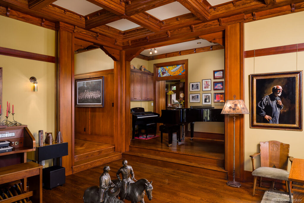 Craftsman-style music room with grand piano, coffered wood ceiling, bronze sculptures, and portrait painting in a Houston residential interior.