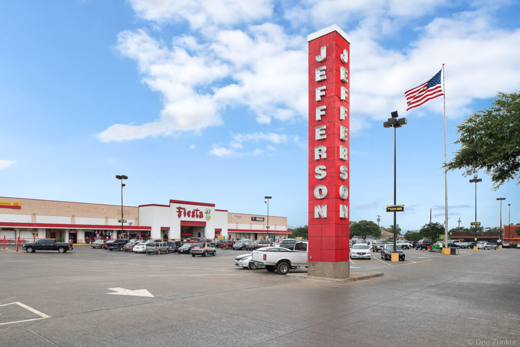 Red tower pylon sign and parking lot of a Dallas TX strip mall shopping center with grocery store anchor tenant.