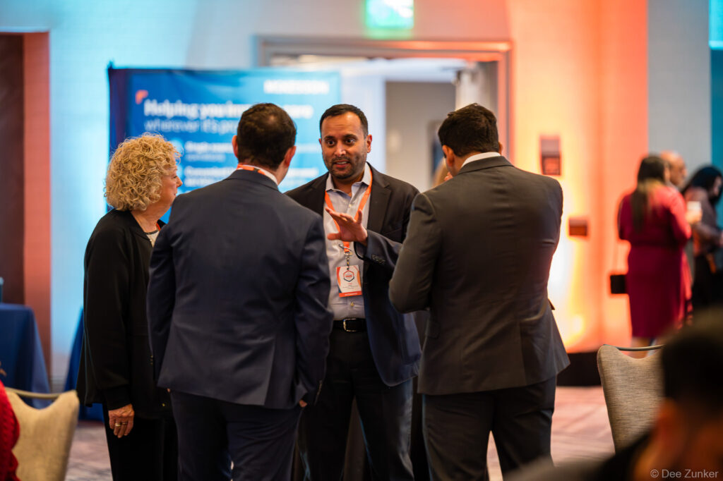 Professionals networking in small group at KabaFusion 2026 conference, Houston hotel ballroom, with event banner visible in background.
