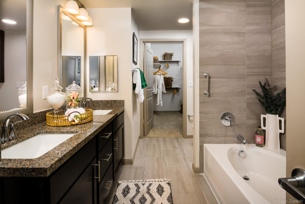 Spacious Katy apartment bathroom with granite double vanity, soaking tub, large tile surround, and walk-in closet beyond