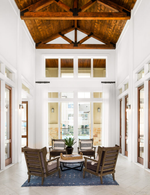 Luxury apartment clubhouse foyer with soaring vaulted wood-beam ceiling, white walls, and elegant seating area in Katy Texas
