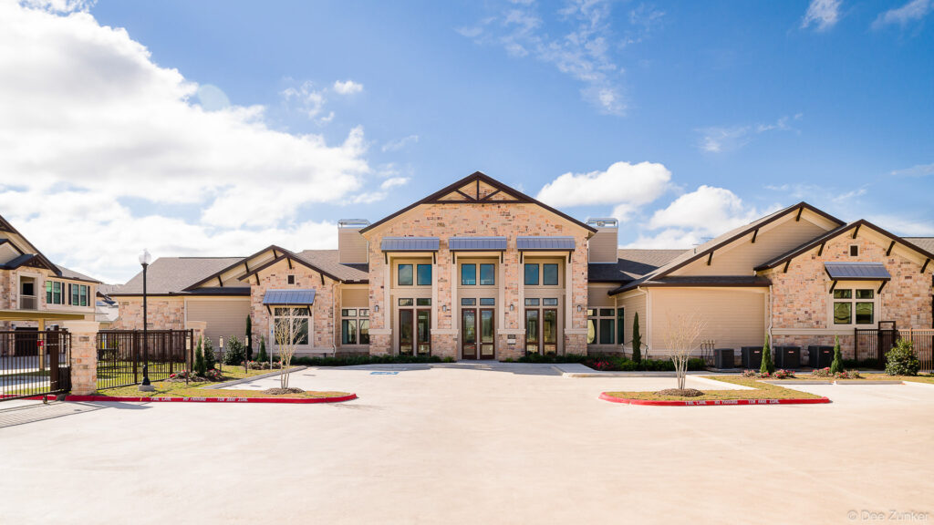 Exterior view of a modern Katy apartment leasing office featuring stone facade, gabled rooflines, and manicured landscaping