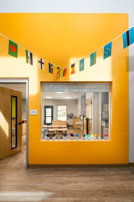 Bright yellow hallway with international flag bunting overlooks a sunlit preschool classroom interior in Austin TX