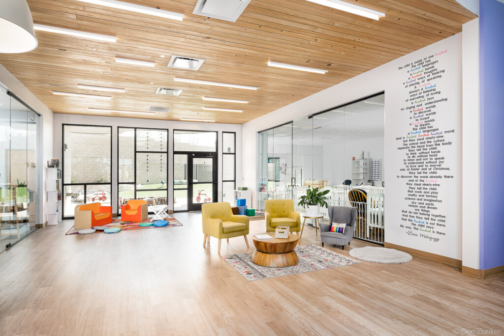 Bright childcare school lounge interior with colorful armchairs, wood-plank ceiling, and inspirational wall quote in Austin TX