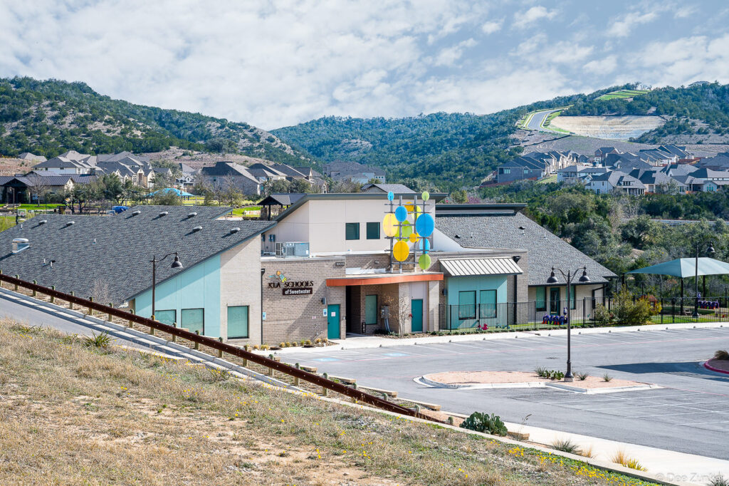 Exterior view of a modern preschool building in Austin TX with colorful circular sculpture accent and Texas Hill Country backdrop