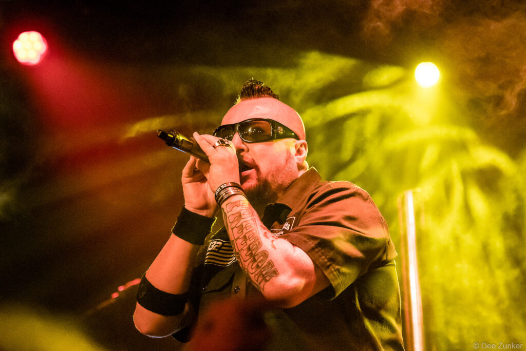 Tattooed male vocalist performs with microphone under dramatic stage lighting at Scout Bar Houston corporate event photography.