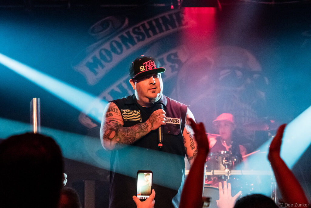 Tattooed male vocalist performs on stage at Scout Bar Houston, holding microphone under dramatic blue and red stage lighting.