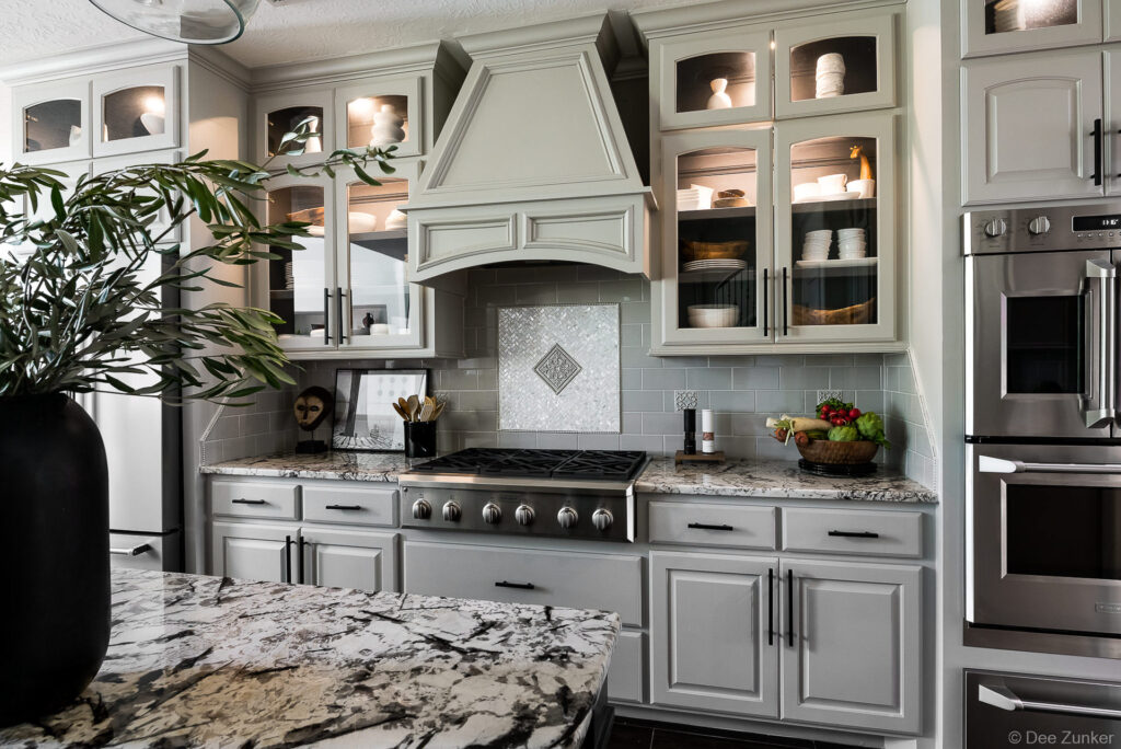 Elegant gray kitchen with marble countertops, custom range hood, glass-front cabinets, and gas cooktop in a Houston luxury home interior.