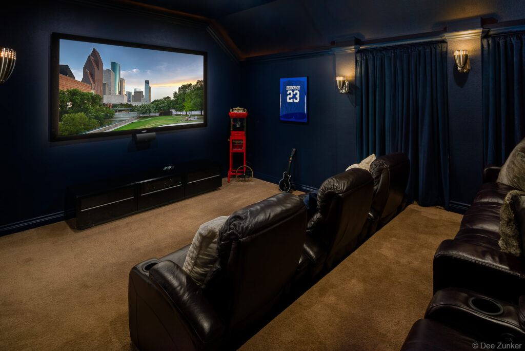 Dark blue home theater room with leather recliners, large screen TV, popcorn machine, and framed sports jersey in Houston residence.