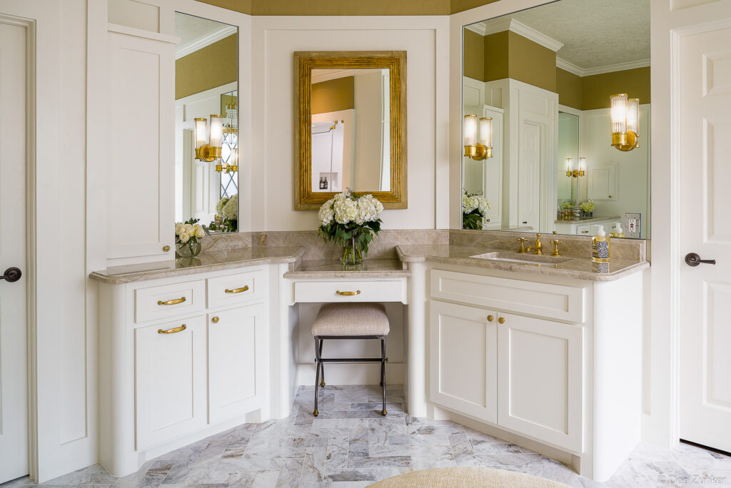 Corner vanity with white cabinetry, gold hardware, marble countertops, hydrangea arrangement, and makeup station in Houston residential interior.