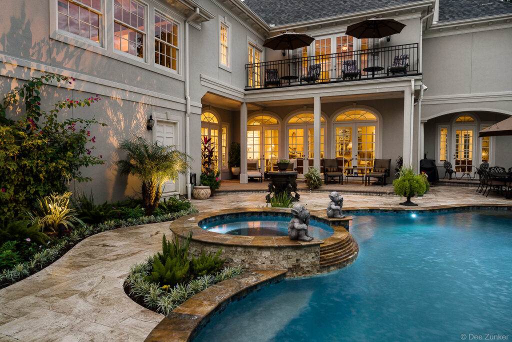 Illuminated luxury backyard pool and spa with stone surround, garden statues, and arched French doors at Sugar Hill Houston residence.