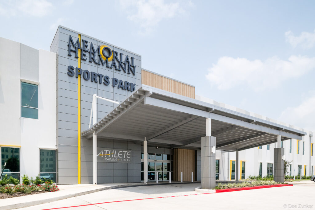 Exterior entrance of a modern Houston sports medicine and athlete training facility with covered canopy and bold signage