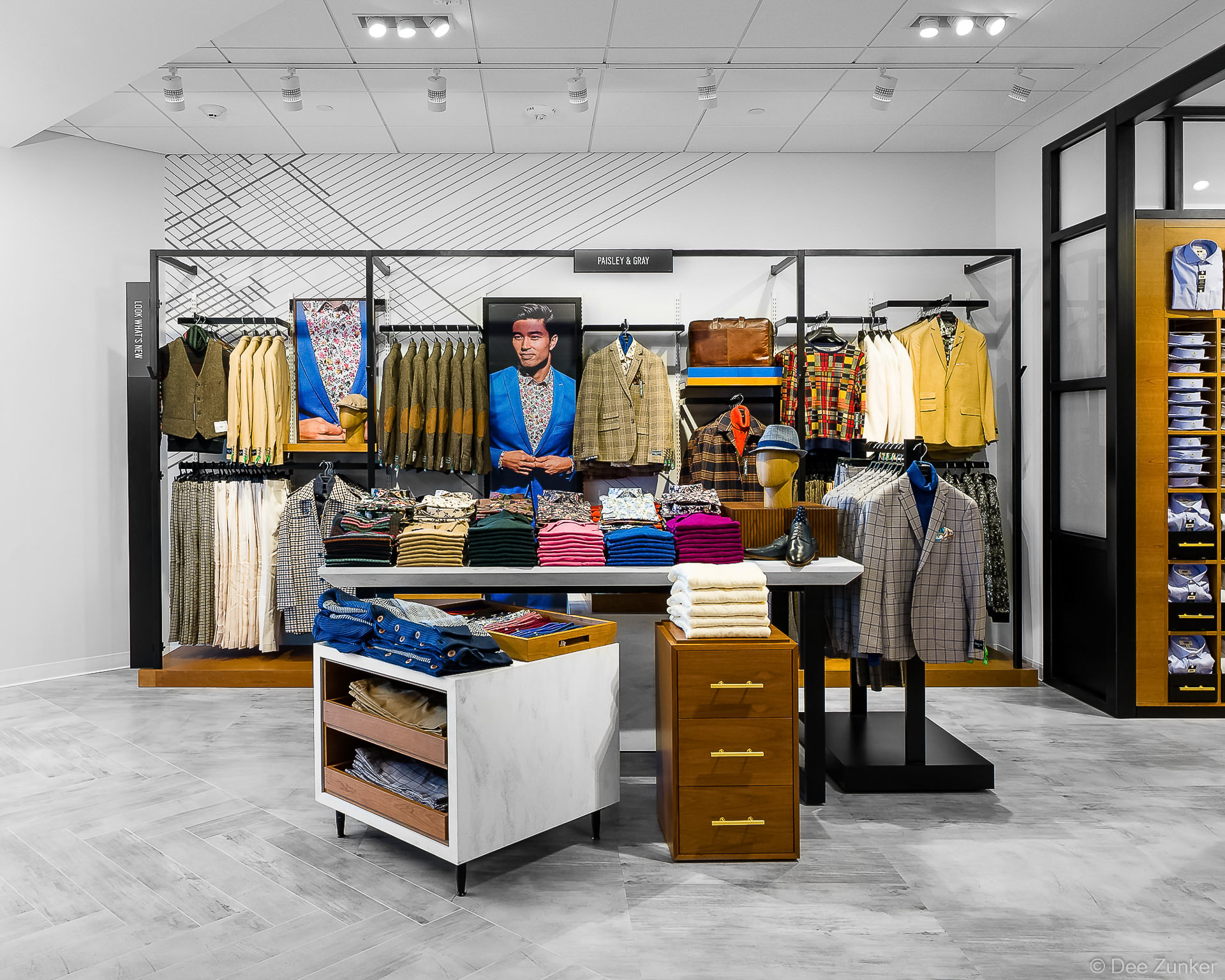 Bright menswear retail interior featuring colorful sport coats, folded shirts, and styled mannequins on modern display fixtures.