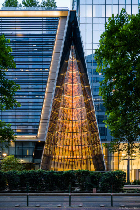 Illuminated triangular glass facade of a modern downtown Houston skyscraper glowing warm amber at dusk, exterior architectural detail