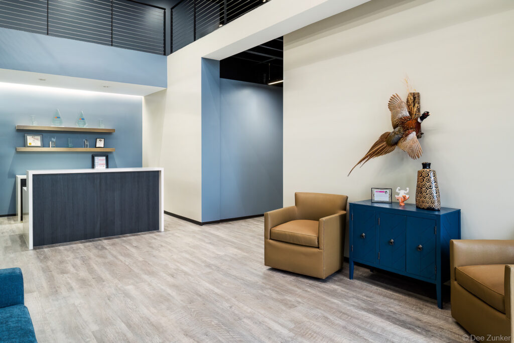 Contemporary office lobby with blue cabinetry, tan leather chairs, reception desk, and mounted pheasant wall decor in Houston commercial space.