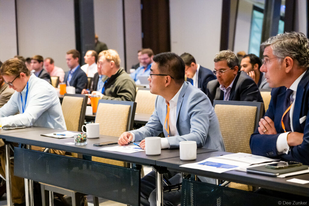 Professional conference attendees in business attire seated at tables, listening attentively during a corporate meeting session in Houston.
