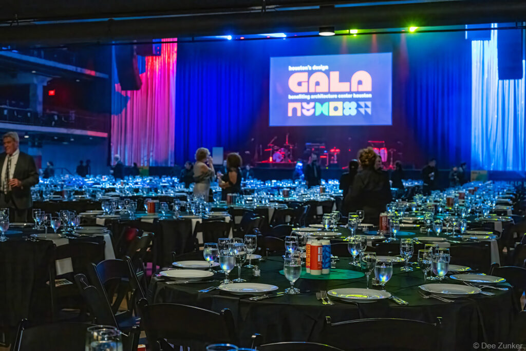 Elegantly set gala dinner tables with glassware fill a Houston event venue ballroom lit in blue with a projected fundraiser logo