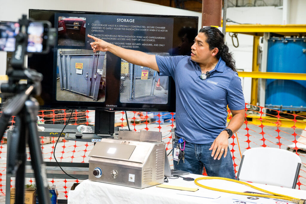 Presenter points to a display screen showing storage vault procedures during Oceaneering Safety Day corporate event in Houston.