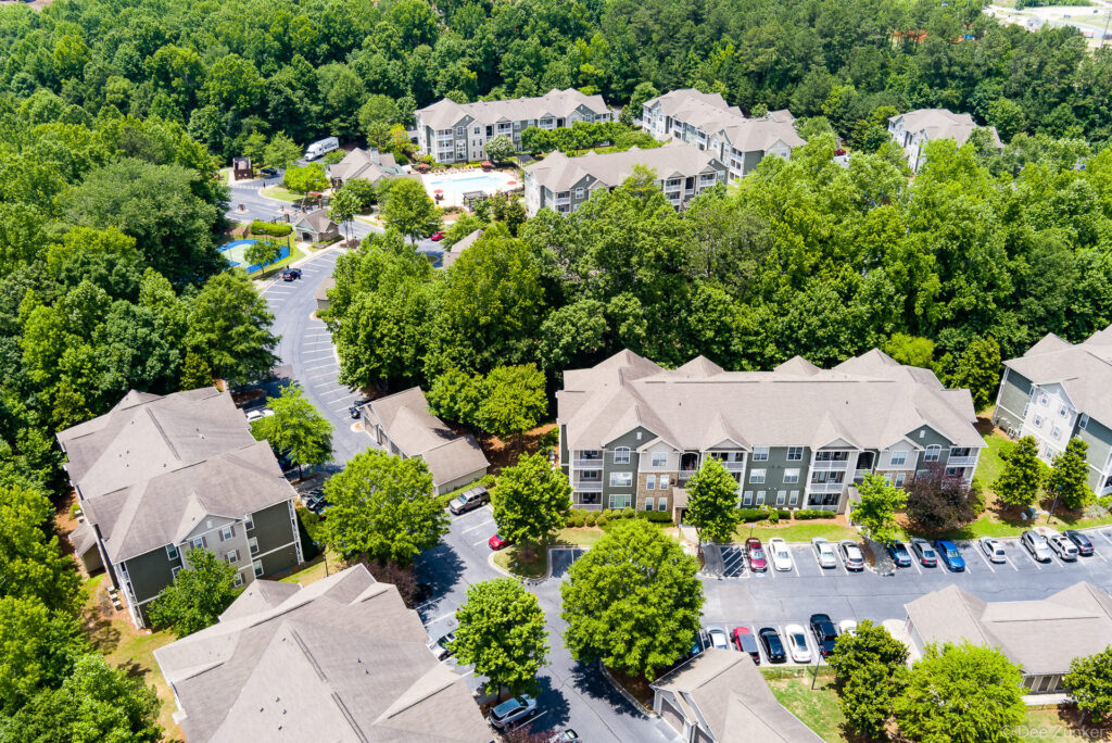 Drone aerial photo of a Georgia apartment complex surrounded by mature trees, showing multi-building layout, parking lots, and pool amenity.
