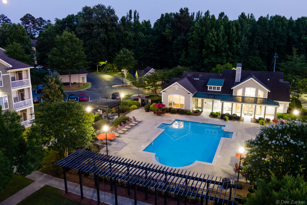 Aerial dusk view of Georgia apartment community pool, clubhouse, lounge chairs, and pergola surrounded by lush trees.