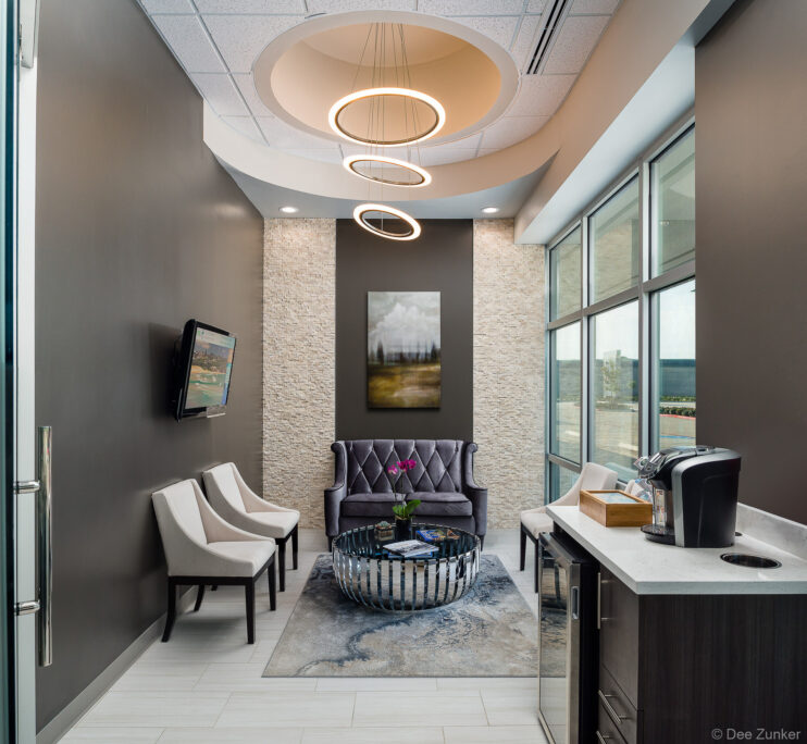 Upscale dental office waiting room with tufted velvet loveseat, ring pendant lights, stone accent wall, and coffee bar in Pearland Texas